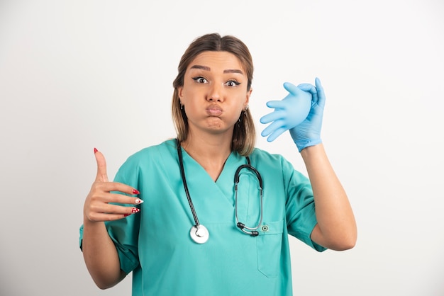 Infirmière souriante portant des gants en latex sur fond blanc.