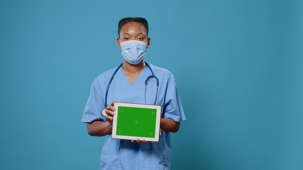 Infirmière tenant une tablette avec écran vert horizontal, portant un masque facial contre le coronavirus. Spécialiste médical utilisant un appareil moderne avec clé chroma, modèle de maquette et arrière-plan isolé.