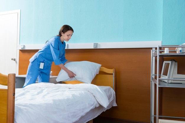 Infirmière tient un oreiller blanc sur le lit d'hôpital dans la salle d'hôpital, la porte de la chambre est fermée derrière son dos. concept de soins de santé
