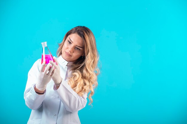 Infirmière en uniforme blanc tenant un flacon de produit chimique avec un liquide rose et le vérifiant.