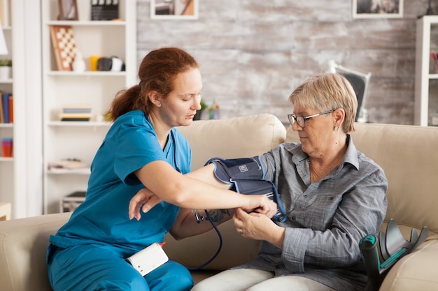 Infirmière utilisant un appareil de pression artérielle numérique sur une femme âgée dans une maison de soins infirmiers.