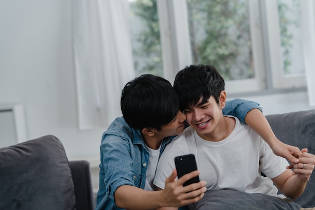 Influenceur asiatique couple gay vlog à la maison. Les hommes LGBTQ asiatiques heureux se détendent en utilisant la technologie en enregistrant des vidéos sur le téléphone mobile en enregistrant des vidéos sur les réseaux sociaux tout en restant allongés dans le salon.
