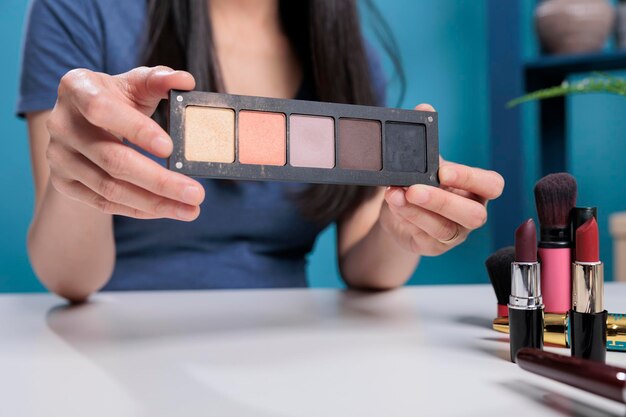 Influenceur des médias sociaux tenant une palette de maquillage faisant un tutoriel d'enregistrement de revue cosmétique pour la chaîne de vlogging en studio. Produit de maquillage attrayant pour les créateurs de contenu. Fermer