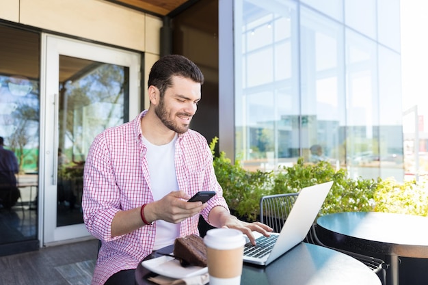 Influenceur souriant partageant des histoires de nourriture en ligne via un smartphone et un ordinateur portable au café