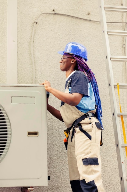 Photo gratuite un ingénieur afro-américain démonte le panneau supérieur en métal du climatiseur extérieur pour vérifier les composants défectueux. technicien certifié effectuant des réparations sur un système de cvc endommagé