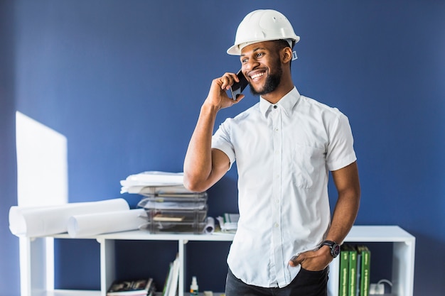 Photo gratuite ingénieur afro-américain heureux, parler au téléphone mobile dans le bureau