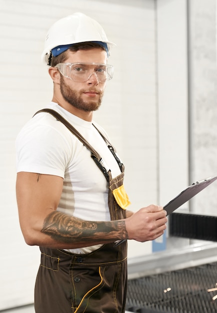 Photo gratuite ingénieur brutal en uniforme tenant le dossier, posant sur l'usine