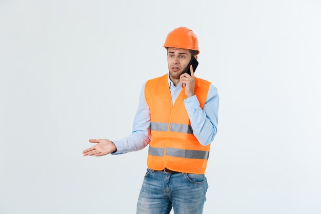 Ingénieur en construction parlant sur téléphone portable, homme adulte sérieux utilisant un smartphone pour communiquer avec les travailleurs sur le chantier.