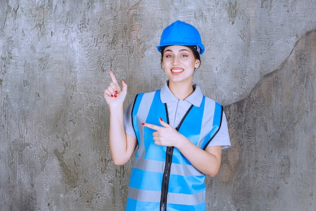 Ingénieur féminin portant un casque bleu et un équipement et pointant quelque chose sur la gauche avec des émotions.