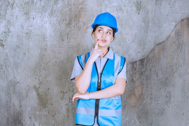 Ingénieur féminin portant un casque et un équipement bleus et pensant ou planifiant