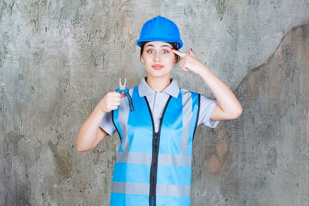 Ingénieur féminin en tenue bleue et casque tenant des pinces pour les travaux de réparation et ayant une idée.