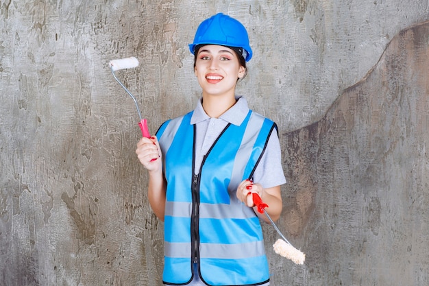 Ingénieur féminin en uniforme bleu et casque tenant un rouleau de finition pour la peinture