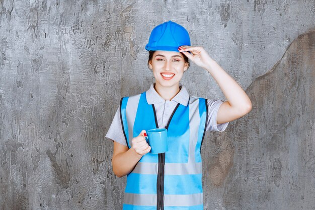 Ingénieur féminin en uniforme bleu et casque tenant une tasse de thé bleu