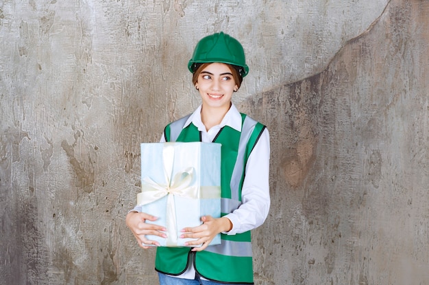 Ingénieur féminin en uniforme vert et casque tenant une boîte-cadeau bleue