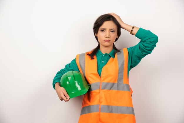 Ingénieur femme bouleversée se gratter la tête et tenant un casque sur fond blanc