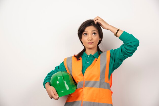 Ingénieur femme se grattant la tête et tenant un casque sur fond blanc.