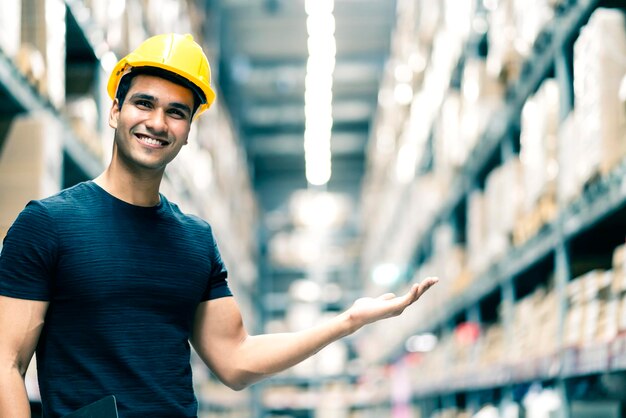 Ingénieur indien intelligent portant un casque de sécurité faisant la vérification des stocks et la gestion des produits de stock de carton dans l'arrière-plan de l'entrepôt de l'usine