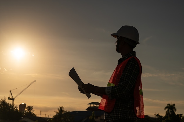 Ingénieur masculin travaillant sur le chantier de construction à l'heure du coucher du soleil de silhouette