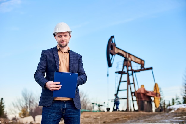 Ingénieur prenant des notes debout dans un champ pétrolifère derrière lui cric de pompe à huile