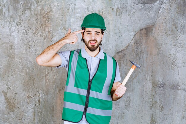 Ingénieur en tenue jaune et casque tenant une hache à manche en bois et semble confus.