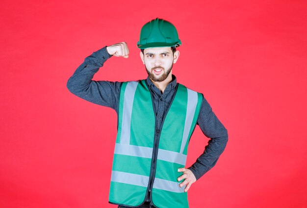 Ingénieur en uniforme vert et casque démontrant son poing.