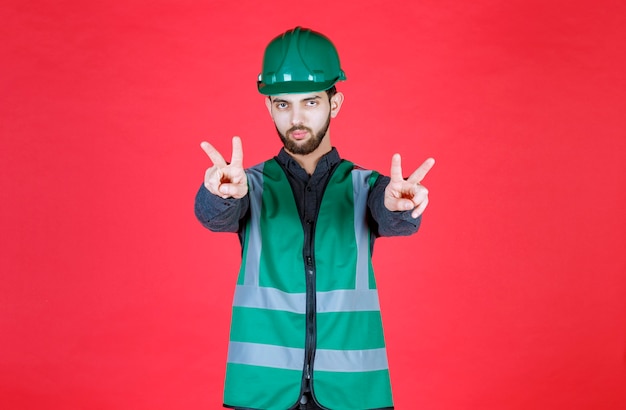 Photo gratuite ingénieur en uniforme vert et casque envoyant la paix et l'amitié.