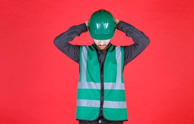 Ingénieur en uniforme vert et casque tenant sa tête alors qu'il est fatigué.