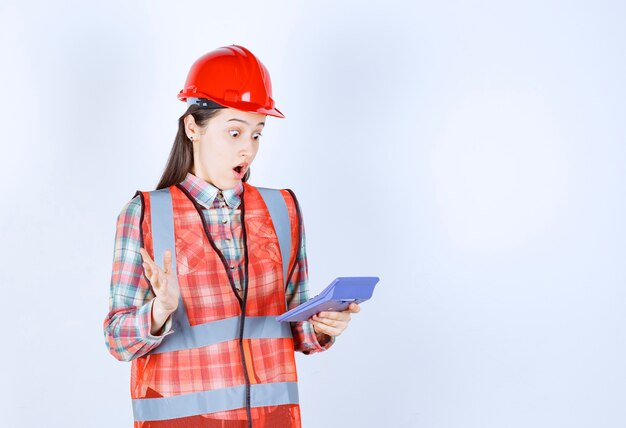 Ingénieure en casque rouge travaillant sur une calculatrice et semble confuse ou ravie.