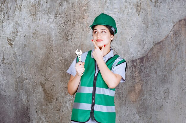 Ingénieure en casque vert tenant une clé métallique pour un travail de réparation et en pensant à de nouvelles idées