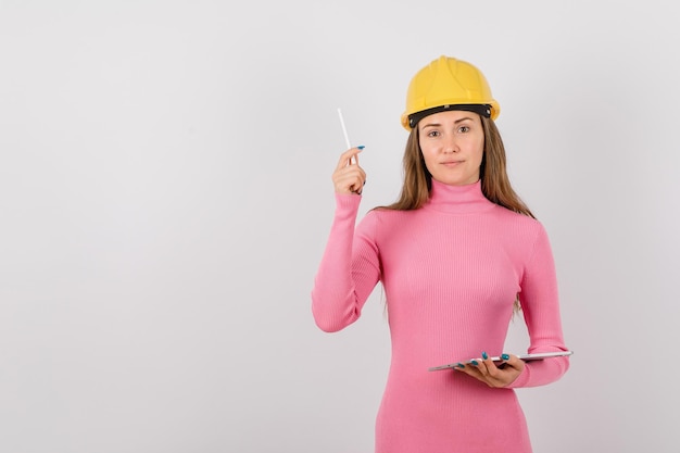 Une ingénieure sérieuse regarde la caméra en levant un stylo sur fond blanc