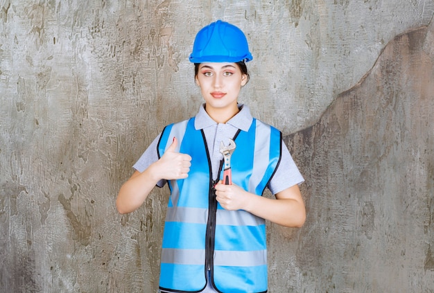 Ingénieure en uniforme bleu et casque tenant une clé métallique.