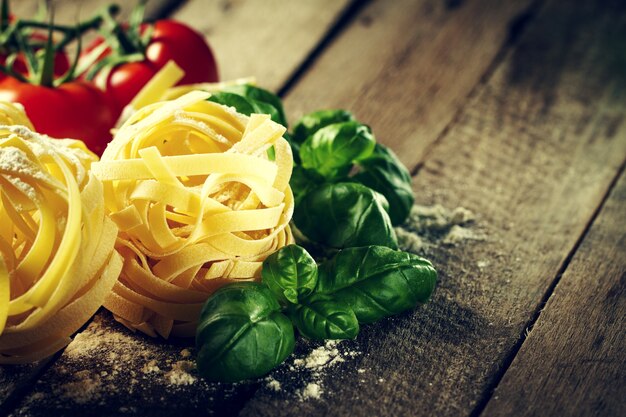 Ingrédients colorés délicieux et frais pour cuisiner des tagliatelles aux pâtes au basilic frais et aux tomates. Fond de table en bois.