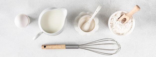 Ingrédients de cuisson oeuf farine sucre lait et ustensiles de cuisine sur fond blanc avec espace pour copier