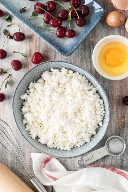 Ingrédients pour faire des boulettes de fromage blanc aux cerises Farine d'oeufs de fromage cottage et cerises fraîches sur une table en bois verticale