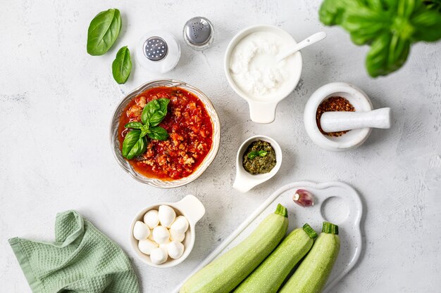 Ingrédients pour des rouleaux de courgettes avec du fromage à la crème et de la sauce tomate sur fond blanc