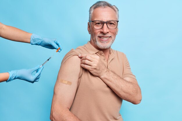 Injection de vaccin contre le coronavirus Un vieil homme heureux étant immunisé contre le covid 19 à l'hôpital lors d'une visite chez un médecin isolé sur un mur bleu porte du plâtre sur le bras Vaccination pour les personnes âgées