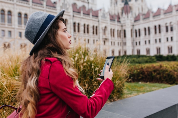 Inquiet femme brune au chapeau gris à l'aide de GPS tout en profitant des attractions