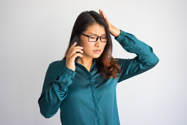 Inquiet jeune femme asiatique parlant au téléphone et touchant la tête.