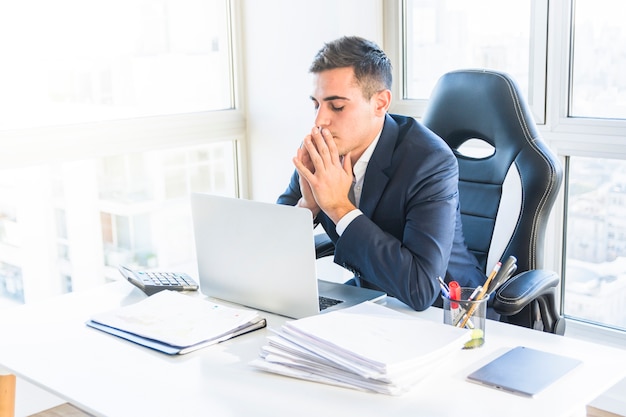 Inquiet jeune homme d&#39;affaires à la recherche d&#39;un ordinateur portable au bureau