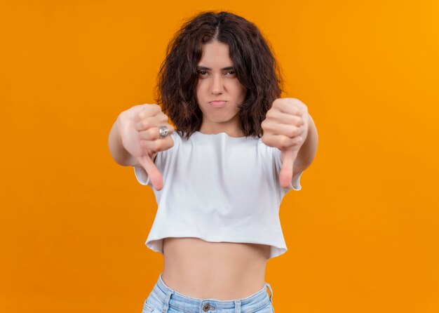 Insatisfait jeune belle fille montrant les pouces vers le bas sur fond orange isolé avec copie espace