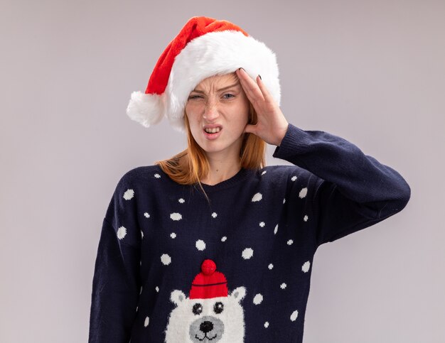 Insatisfait jeune belle fille portant un chapeau de Noël mettant la main sur le front isolé sur fond blanc