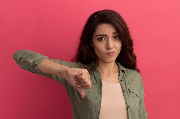 Photo gratuite insatisfait jeune belle fille portant un t-shirt vert olive montrant le pouce vers le bas isolé sur un mur rose