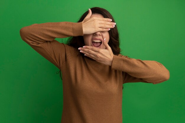 Insatisfait jeune belle fille visage couvert avec les mains isolées sur le mur vert