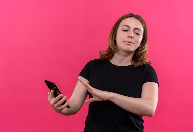 Insatisfait jeune femme décontractée tenant un téléphone mobile et faisant des gestes non sur un mur rose isolé