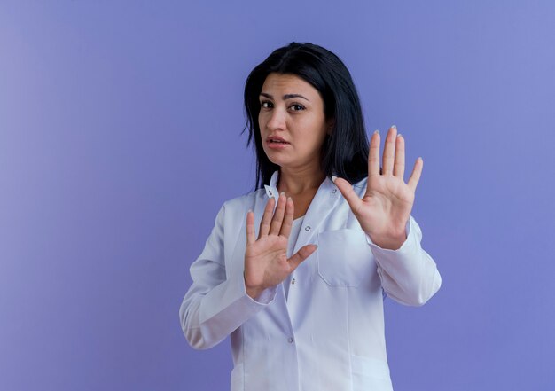 Insatisfait jeune femme médecin portant une robe médicale ne faisant aucun geste isolé sur un mur violet avec copie espace