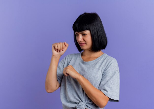 Insatisfait jeune femme de race blanche brune garde les poings à côté isolé sur fond violet avec copie espace