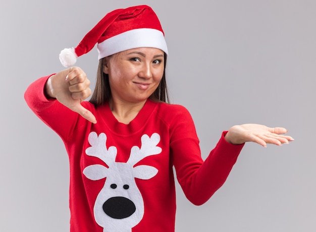 Photo gratuite insatisfait jeune fille asiatique portant chapeau de noël avec chandail montrant le pouce vers le bas isolé sur fond blanc