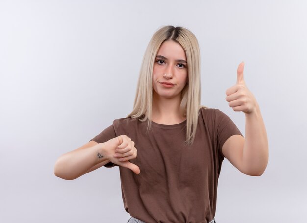 Insatisfait jeune fille blonde montrant les pouces de haut en bas sur un mur blanc isolé