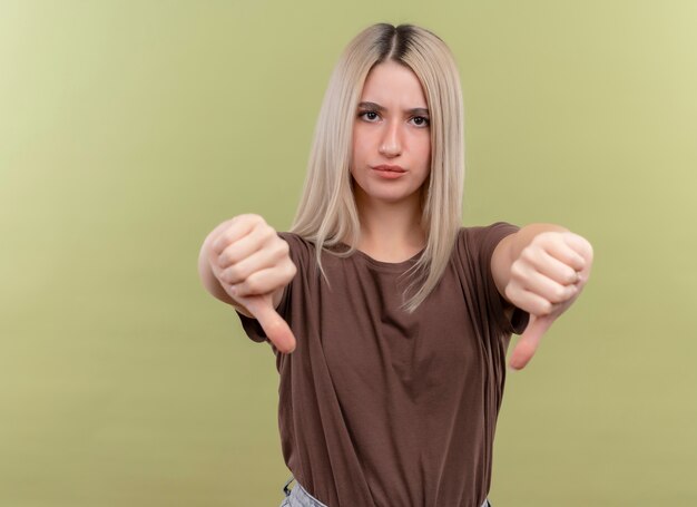 Insatisfait jeune fille blonde montrant les pouces vers le bas sur un mur vert isolé avec copie espace