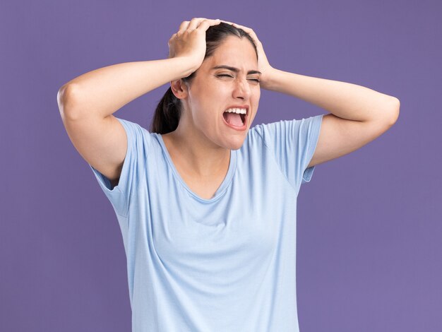 Insatisfait jeune fille caucasienne brune met les mains sur la tête sur le violet